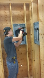 Student using a drill to install an electrical panel.