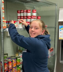 Angela Curtis, Caring Cupboard Assistant, straightens up shelves and greets fellow students with a smile.  